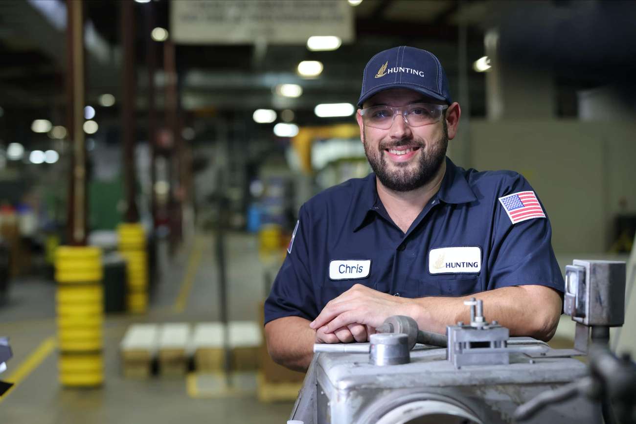 Person with blue hat and shirt with Hunting logos leaning on machine smiling in camera