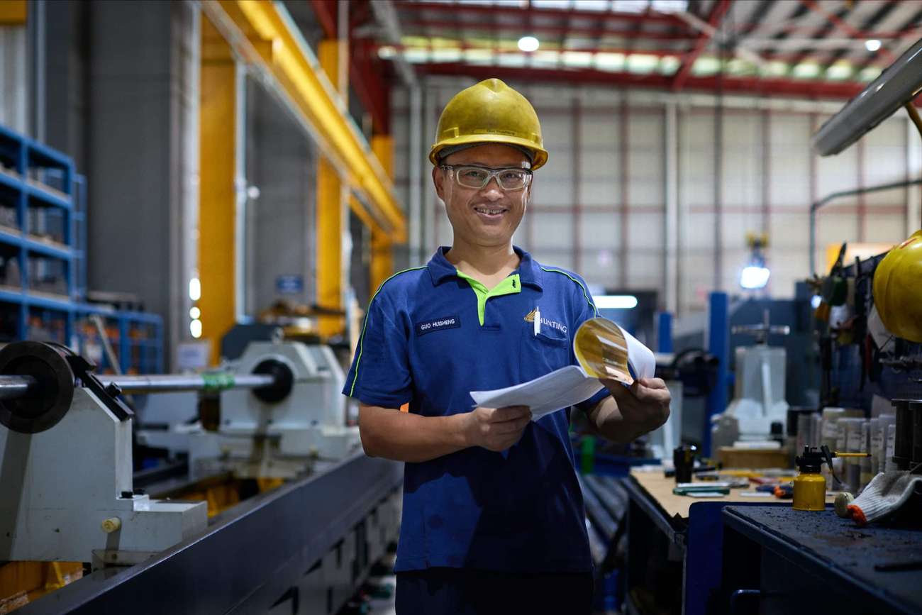 Person with hard hat and protective googles standing in industrial facility smiling in camera